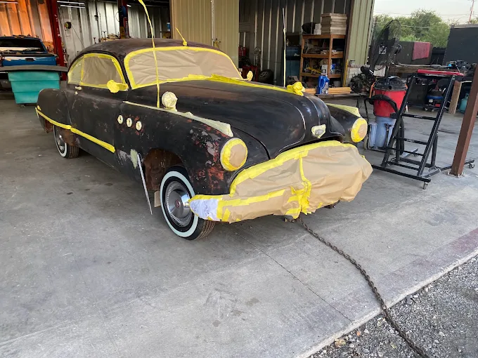 Classic car covered in masking tape and paper inside the shop before painting