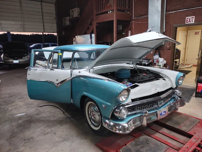 The same style of classic car with finished blue-and-white paint, hood open, inside the shop